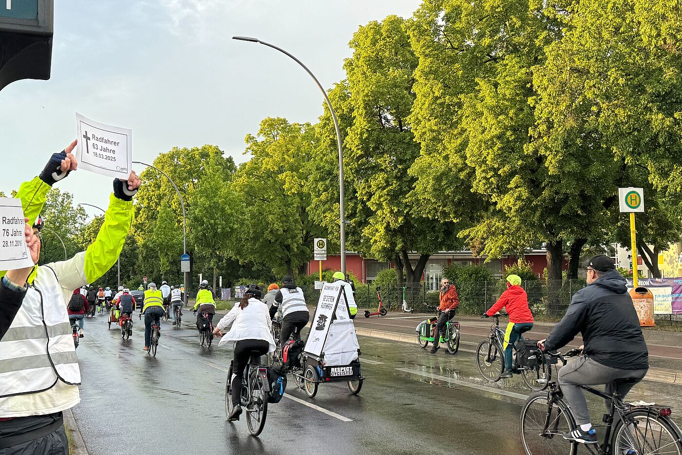 Menschen halten zwei weiße Gedenkschilder bei Fahrraddemonstration in die Luft