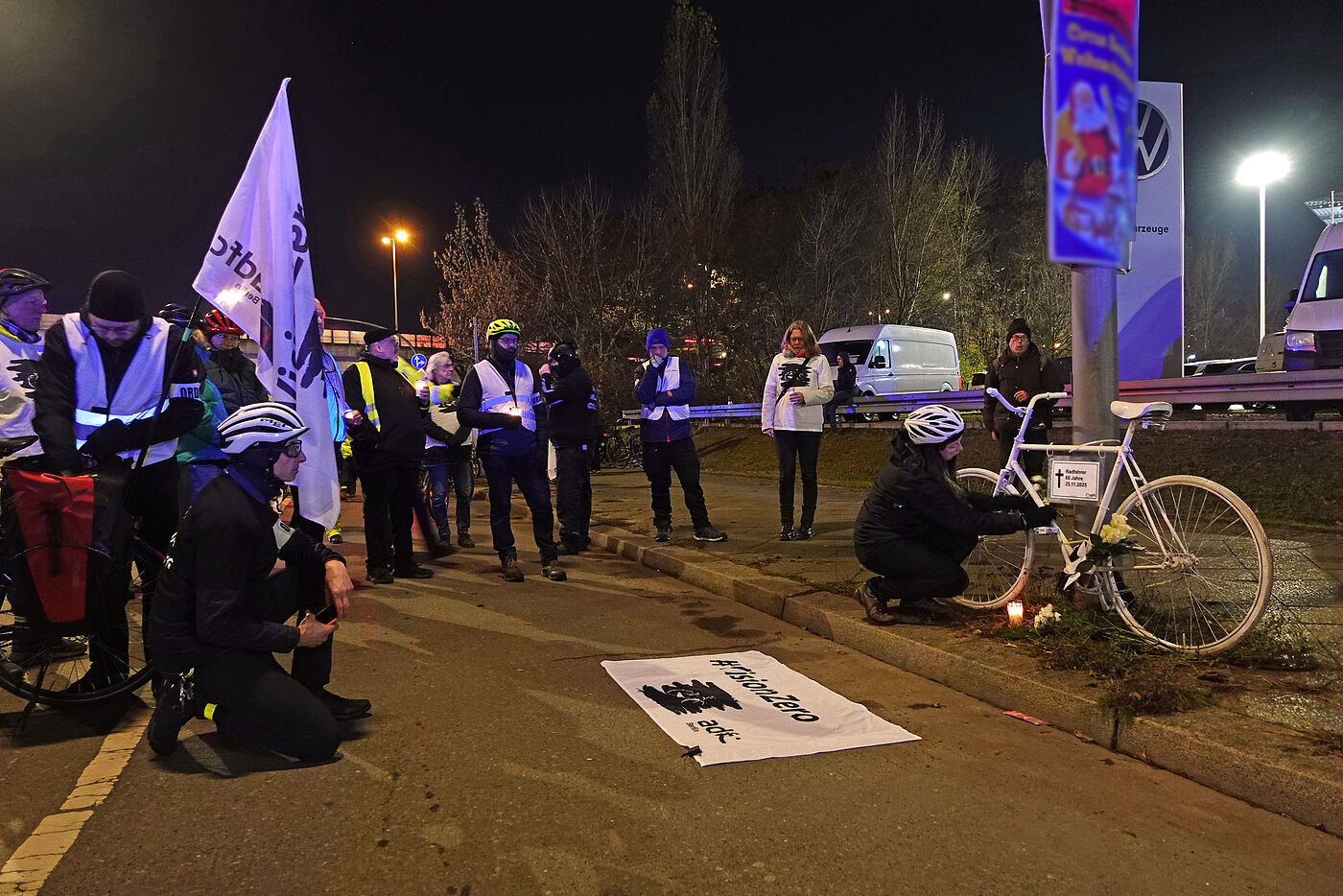Menschen stehen bei einer Vision Zero Wahnwache auf der Straße vor einem weißen Fahrrad