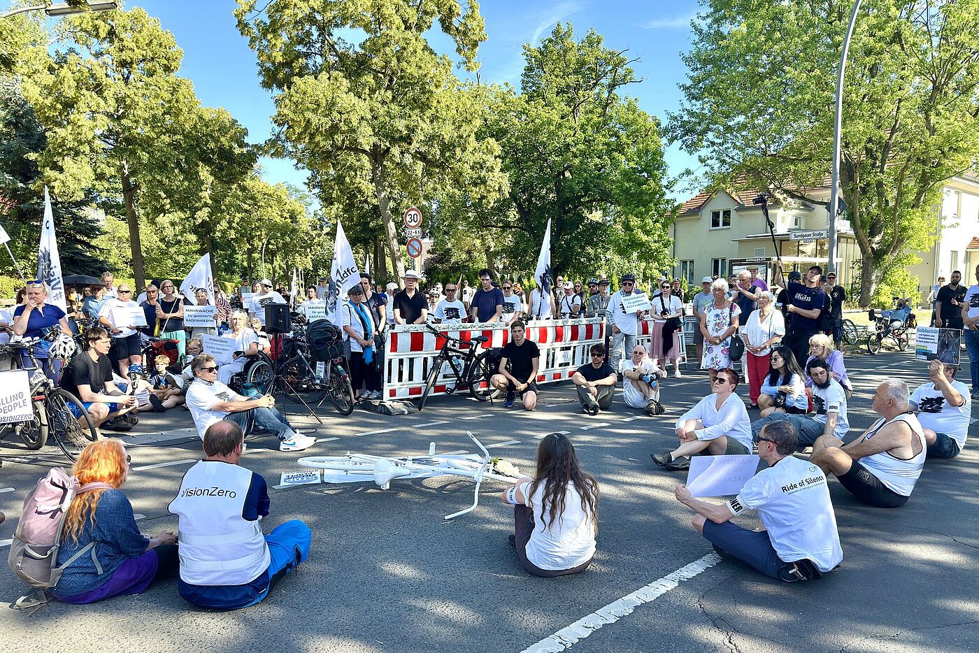 Menschen in weißen Vision Zero T-Shirts sitzen bei einer Mahnwache auf der Straße