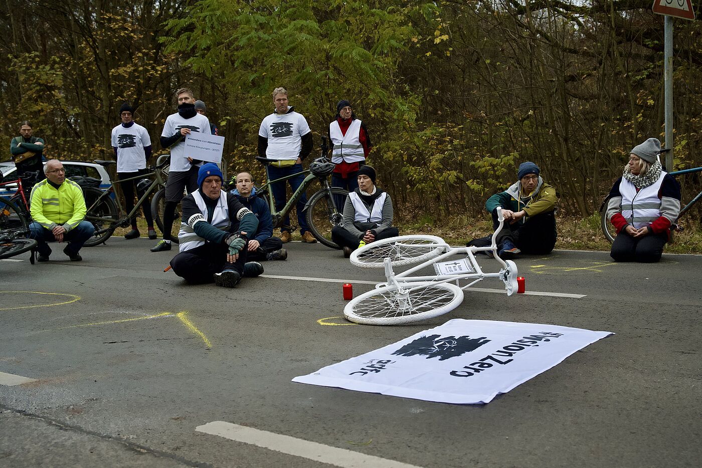 Menschen sitzen zur Mahnwache auf der Fahrbahn, in der Mitte liegt ein weißes Geisterrad