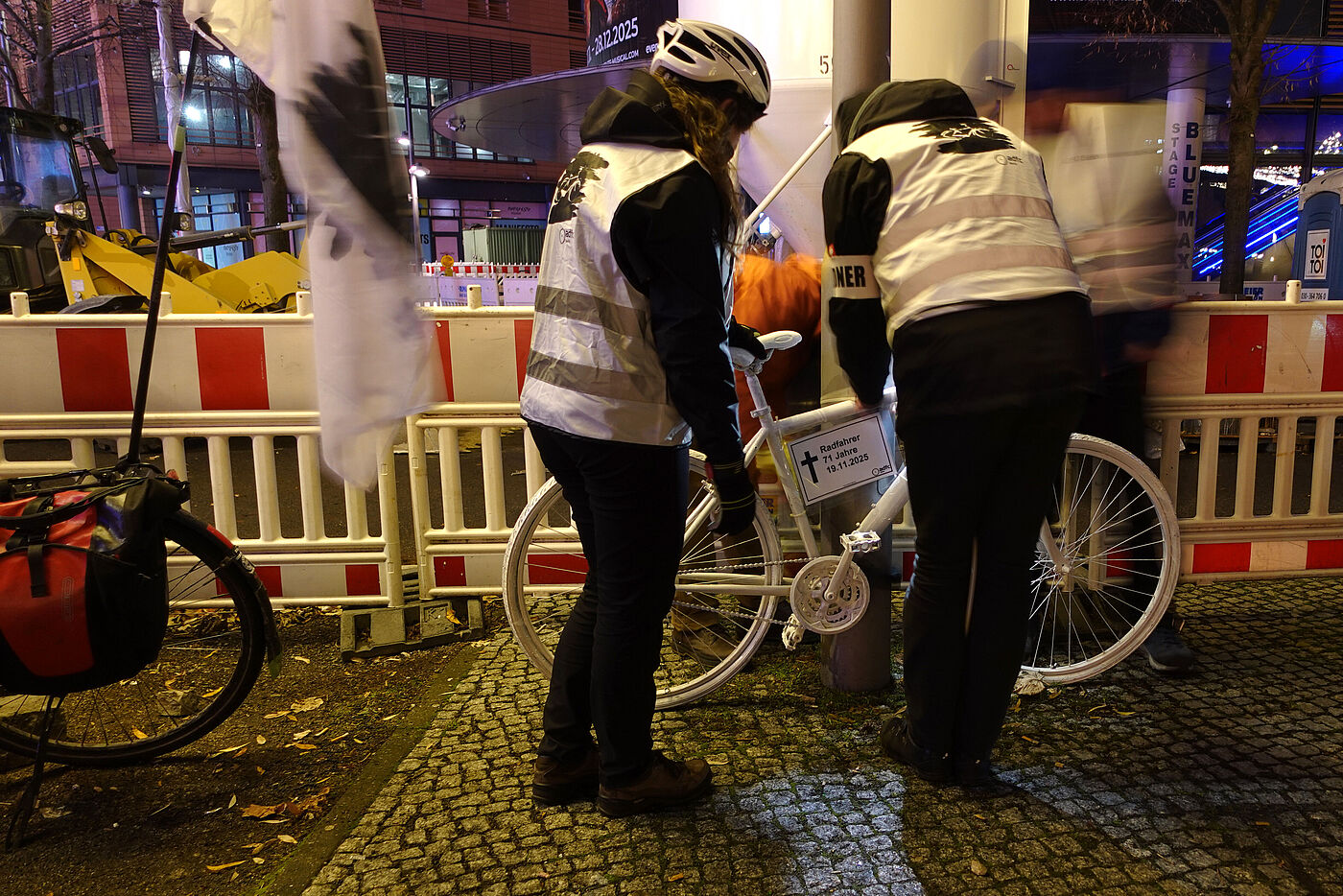 ein weißes Geisterrad wird von Menschen mit weißer Warnweste an einem Laternenpfahl angebracht