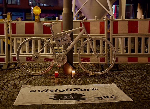 Ein weißes Geisterrad an einem Laternenphal davor eine weiße Vision Zero Fahne