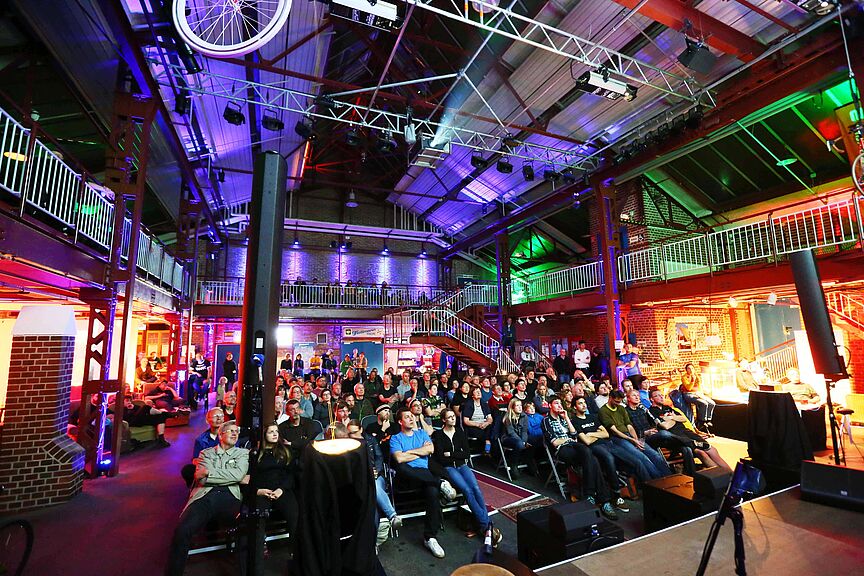 Internationales Fahrrad-Filmfestival Das Bild zeigt das Publikum des Cycling Film Festival, die sitzend auf Stühlen einen Film schauen.